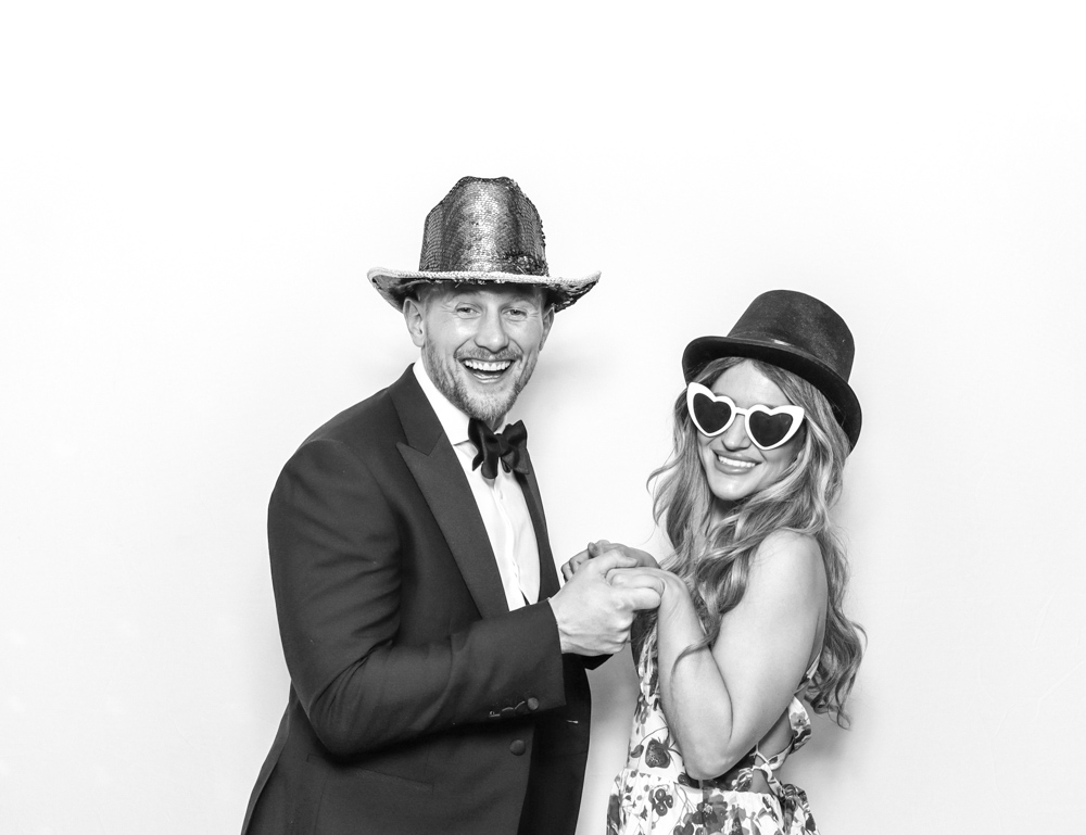 Well-dressed couple wearing sequin and top hats, smiling and holding hands in a digital photo booth with a clean white background.