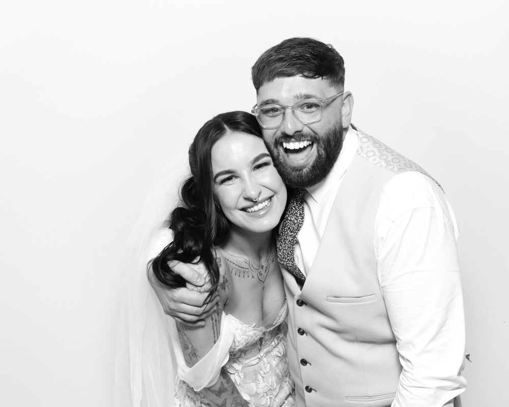Bride and groom laughing together during their wedding photo booth session, in classic black and white style.