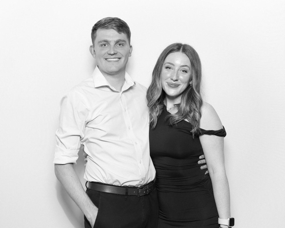 Smartly dressed couple posing closely in a minimalist digital photo booth setup.