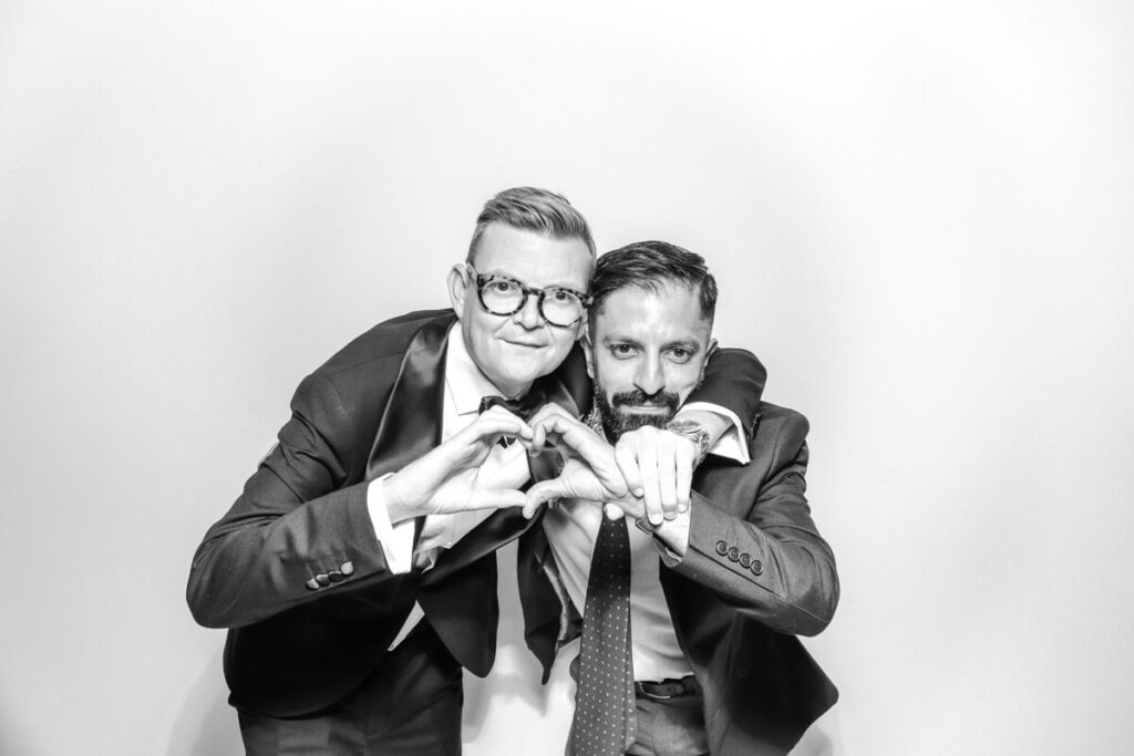 Two groomsmen creating a heart shape with their hands in the black and white photo booth during a wedding at Kiftsgate Court Gardens.