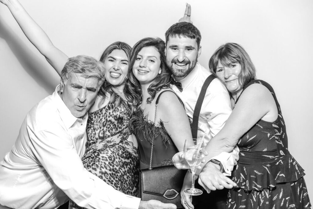 A lively group of five wedding guests posing together with drinks and big smiles in the photo booth at a Kiftsgate Court Gardens marquee wedding.