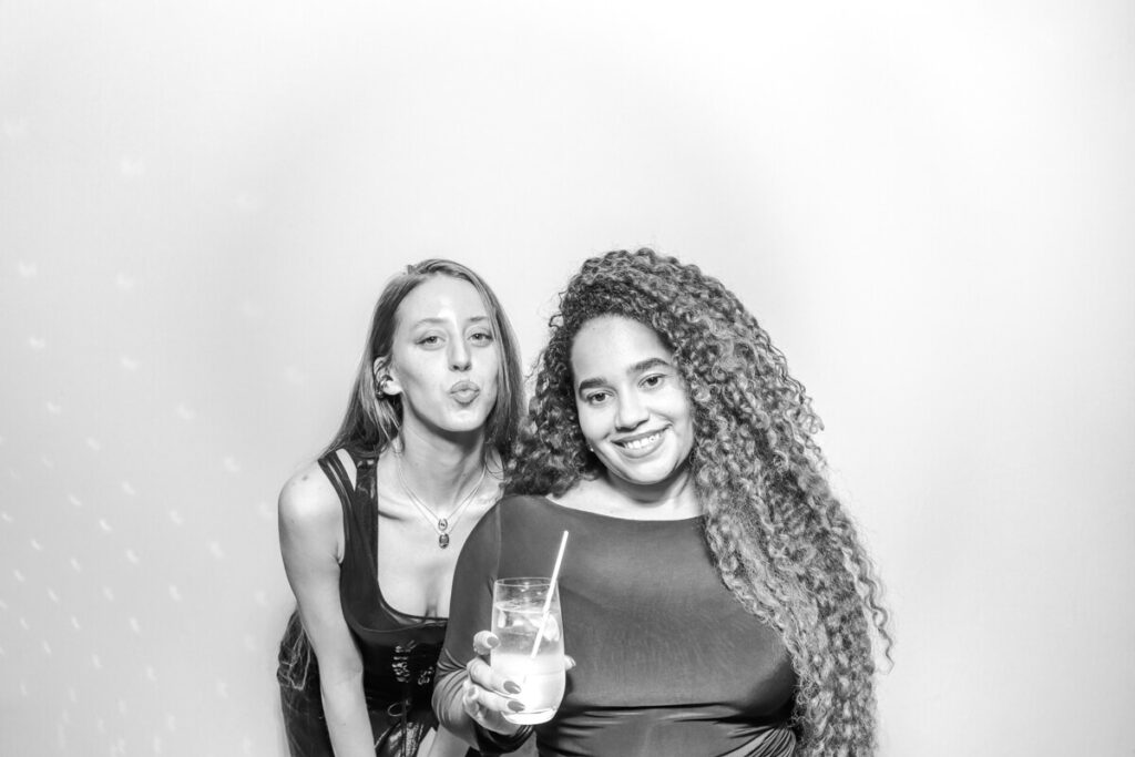 Two guests smiling and posing in the black and white photo booth at a Kiftsgate Court Gardens wedding near Chipping Campden, one holding a cocktail.
