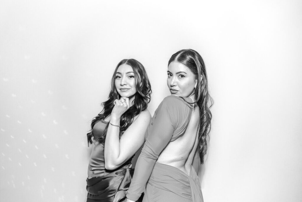 Two stylish female guests posing confidently in the black and white photo booth during an evening reception at Kiftsgate Court Gardens.