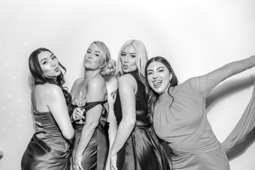 Four female guests striking playful poses in the black and white photo booth for a chipping campden private wedding
