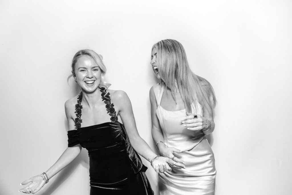 Two female wedding guests laughing together in the black and white photo booth wedding.