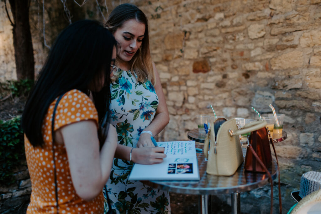 2 guests writing in the custom wedding guest book during an outdoor wedding reception entertainment