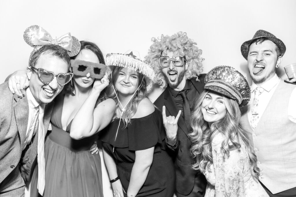 one male guest posing with a wig prop on his head, posing against a white backdrop with a b&w filter for kardashian style selfie pod hire for a party photo booth hire affordable party entertainment