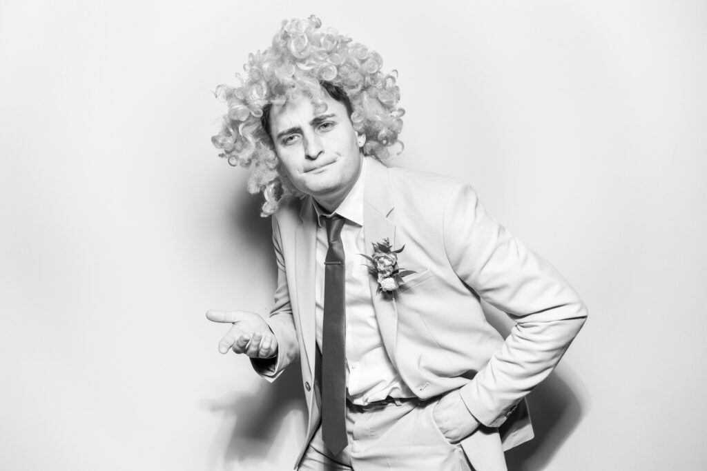 one male guest posing with a wig prop on his head, posing against a white backdrop with a b&w filter for kardashian style selfie pod hire for a cheltenham photo booth hire affordable party entertainment