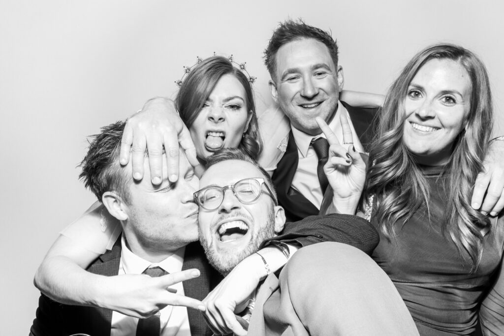 large group pf people posing and kissing eachother, with a plain white backdrop and a b&w filter for kardashian style selfie pod hire for a cheltenham photo booth hire affordable party entertainment