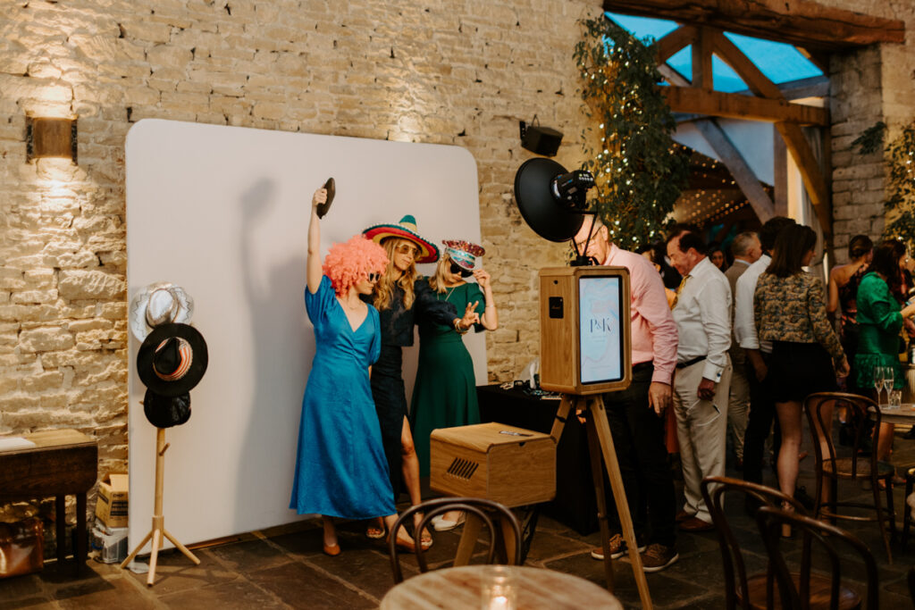 setup of the icon wooden photo booth setup with guests posing wearing party props, posing against a white backdrop for the kardashian style b&w prints