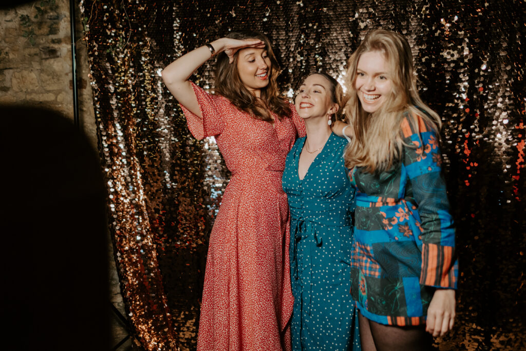 3 guests posing for a photo booth with a champagne sequins backdrop in the back, for an outdoor photo booth hire