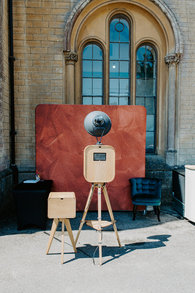Retro photo booth setup with a maroon backdrop for an outdoor garden party at Grittleton House wedding venue in Wiltshire 

