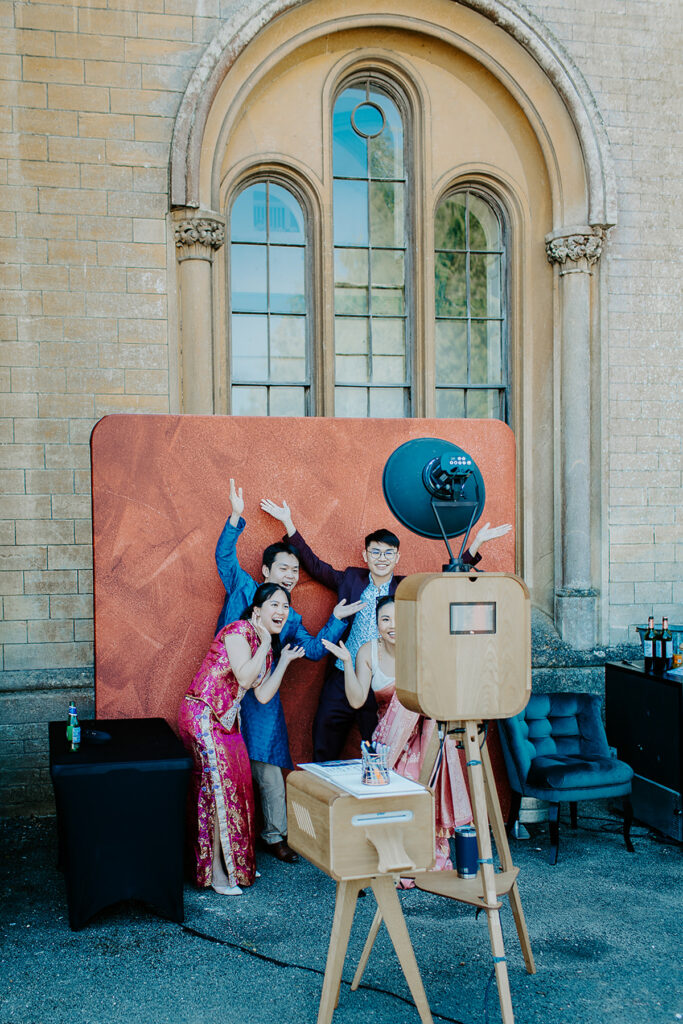 wooden outdoor photo booth with maroon backdrop for an outdoor asian wedding in the summer at grittleton house near Bath
