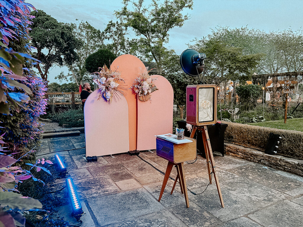 wooden outdoor photo booth with summer arches backdrop during an outdoor garden party in the summer in cotswolds