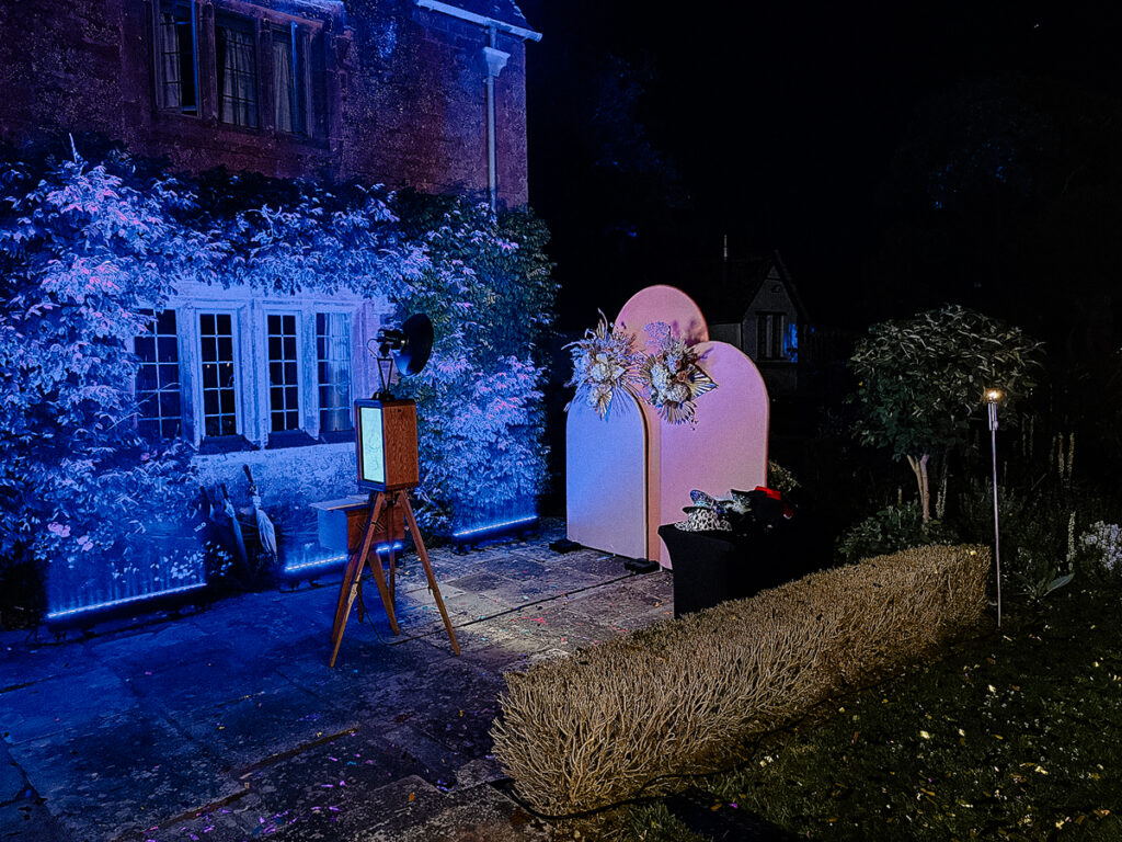 wooden outdoor photo booth with summer arches backdrop during an outdoor garden party in the evening summer in cotswolds