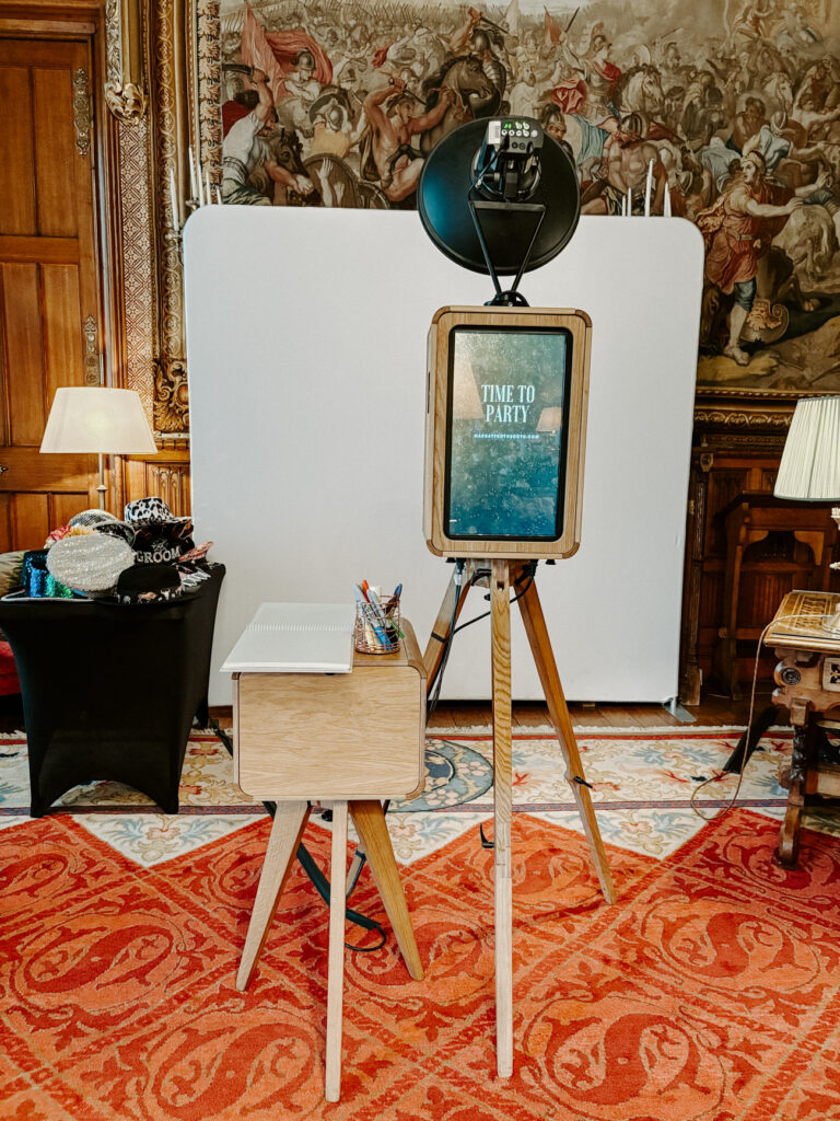 The Icon Photo Booth set up at Eastnor Castle with a white backdrop, guestbook station, and props. Wooden design and studio lighting for stylish black and white prints.