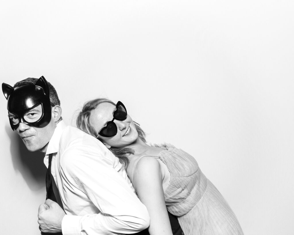 Photo booth snap of a couple having fun in black & white. Wearing cat and heart-shaped masks with a clean white backdrop.