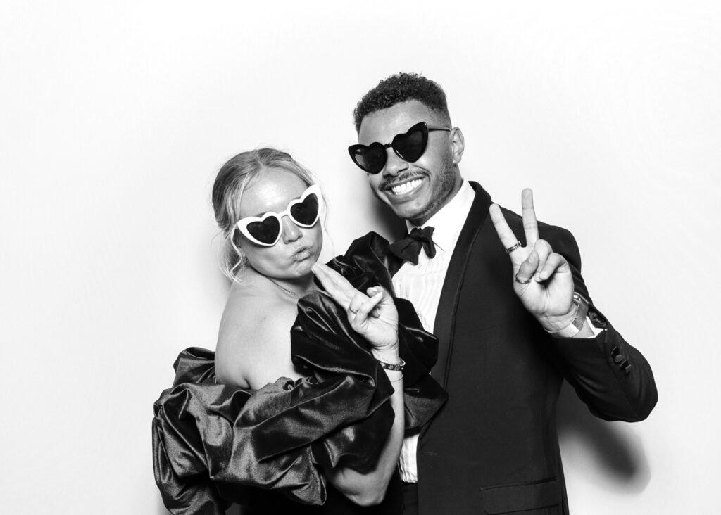 Guests at Eastnor Castle pose in heart-shaped sunglasses, flashing peace signs in a fun black and white photo booth moment.