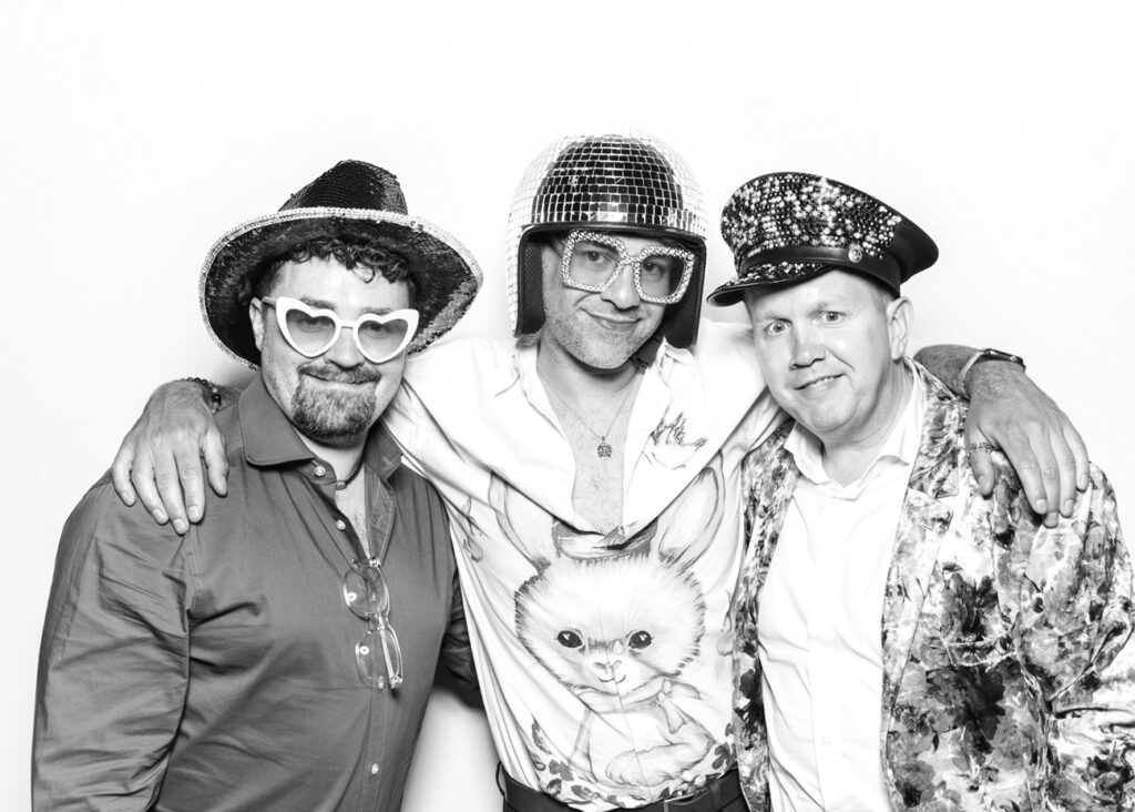 Three guests at Eastnor Castle dressed in playful sequinned hats and party shirts, enjoying the stylish photo booth setup.
