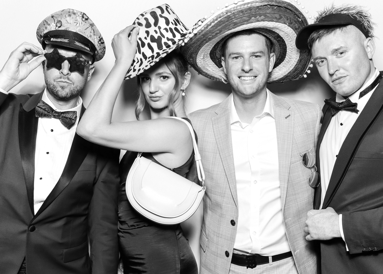 Group of guests dressed in formalwear and playful hats striking poses in a black & white photo booth session for Eastnor Castle wedding party entertainment with Mad Hat Photo Booth hire