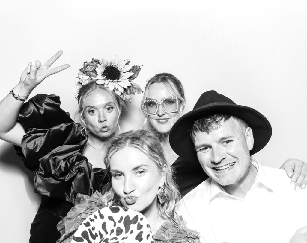Four guests in statement accessories, including a sunflower headpiece and sequin glasses, enjoying the elegant photo booth setup for an Eastnor Castle wedding
