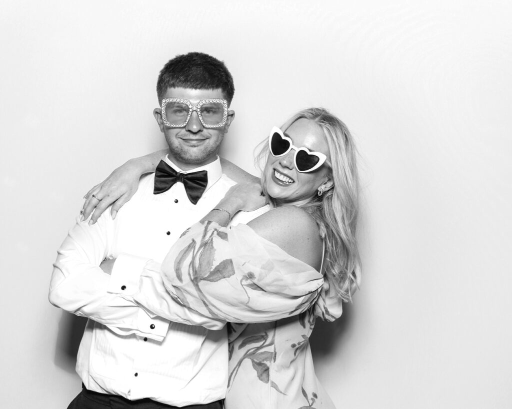 Couple dressed for the occasion, posing with heart-shaped and gem-studded glasses against the clean white backdrop.