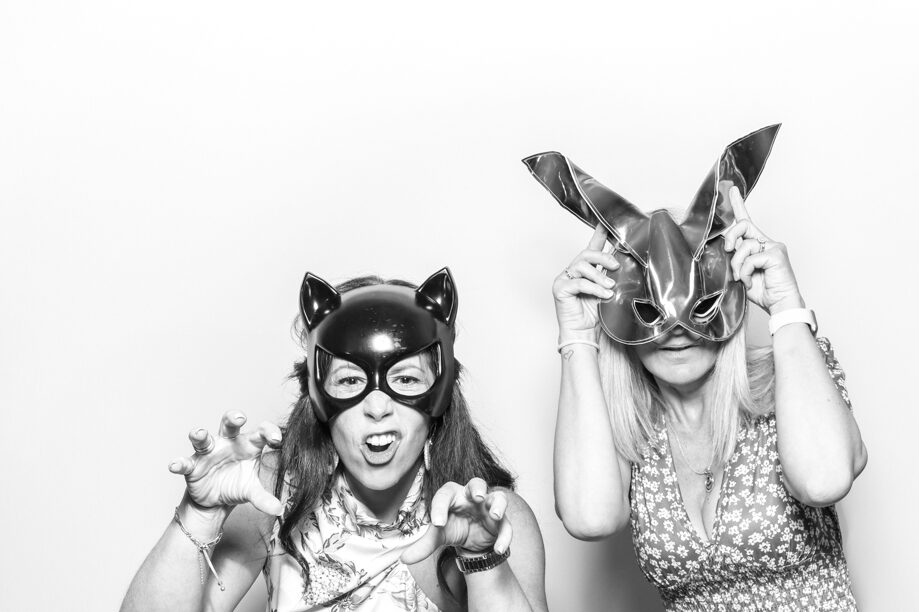 black and white image of 2 guests posing against a white backdrop for photo booths hire near me with a kardashian style look , for a cotswolds wedding venue