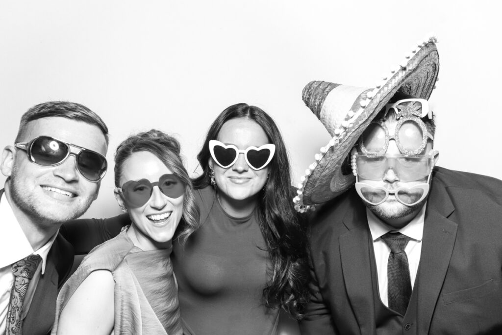 black and white image of a group of guests posing against a white backdrop for the best party entertainment with
kardashian style look , at a cotswolds wedding venue