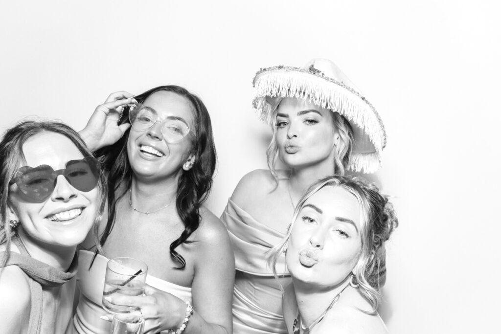black and white image of a group of ladies posing against a white backdrop for photo booths hire near me with a kardashian style look , for a cotswolds wedding venue