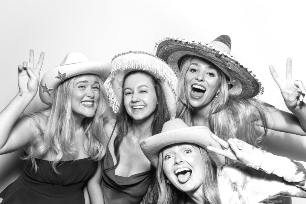 black and white image of a group of ladies posing against a white backdrop for photo booths hire near me with a kardashian style look , for a cotswolds wedding venue