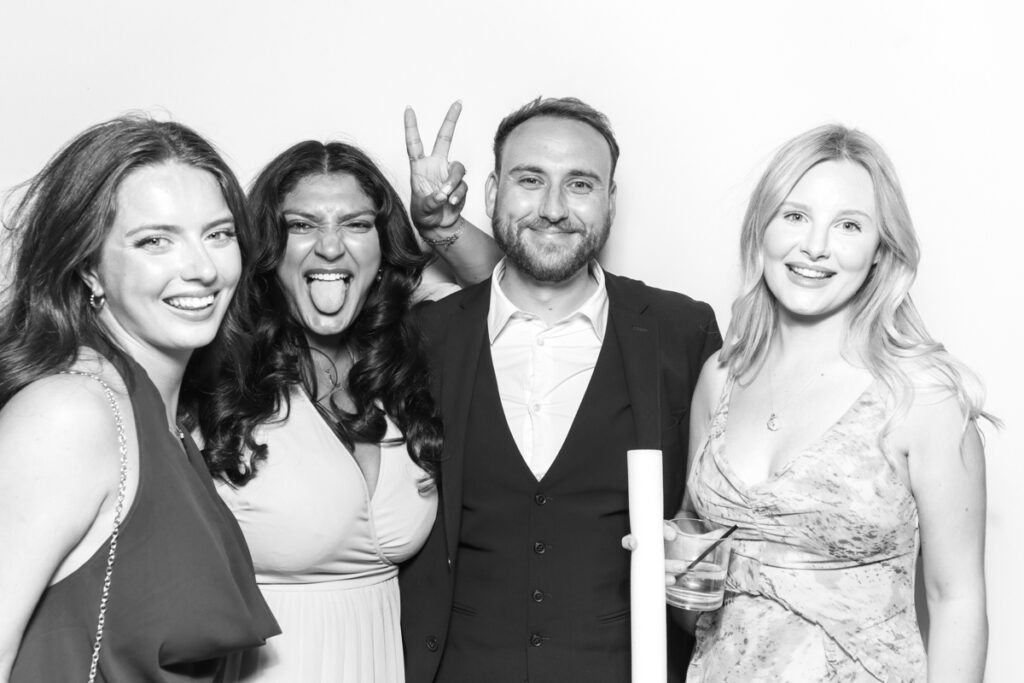 black and white image of a group of guests posing against a white backdrop for a photo booth hire near me with a kardashian style look , for a cotswolds wedding venue
