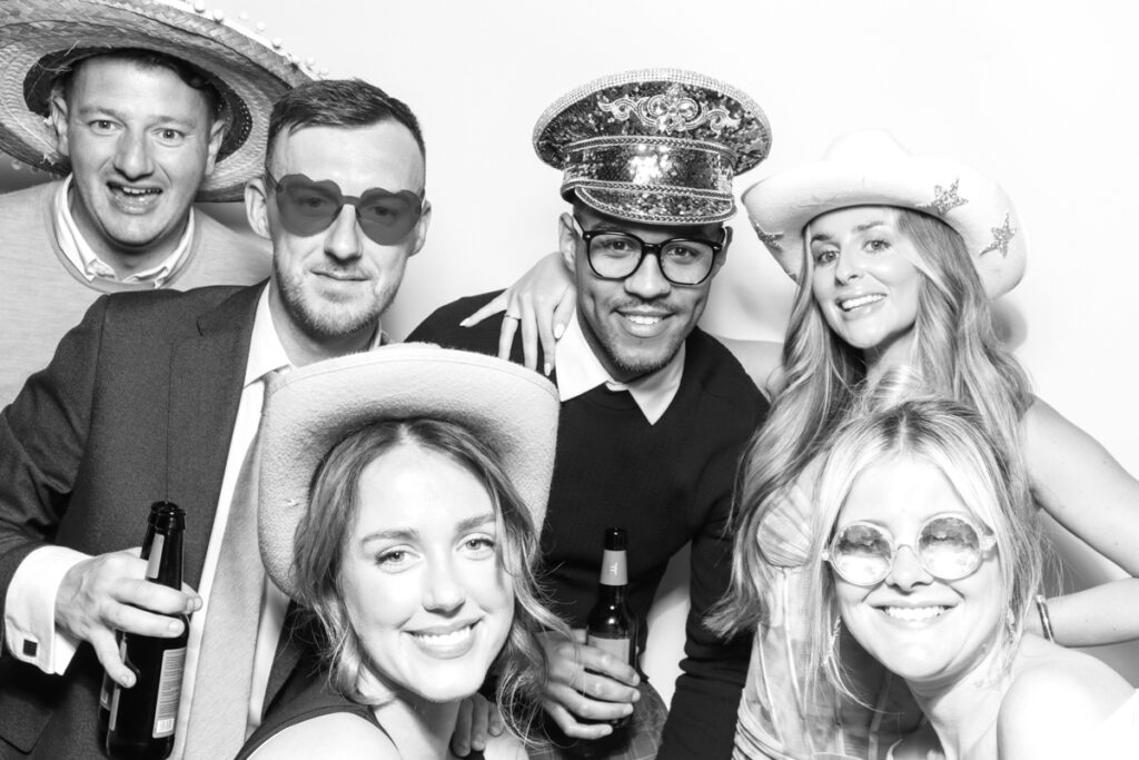black and white image of large group of guests posing with whitefun props for photo booths for hire with a kardashian style look , for a cotswolds wedding venue
