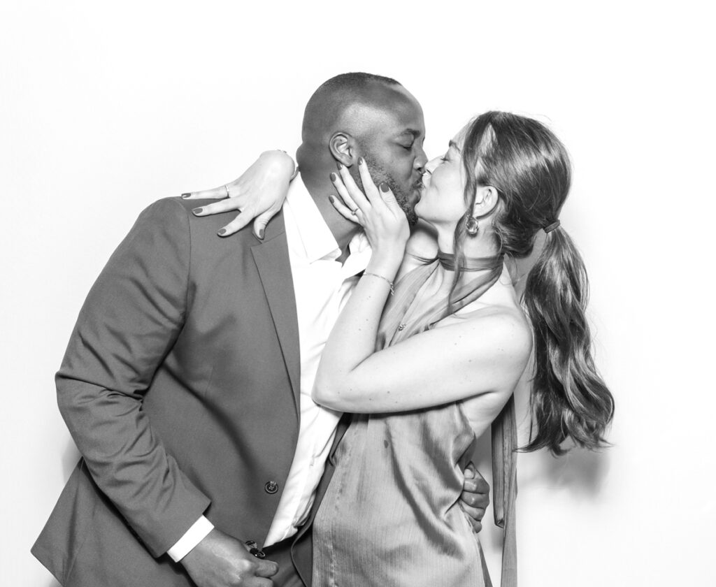 black and white image of 2 guests kissing against a white backdrop for photo booths hire with a kardashian style look , for a cotswolds wedding venue