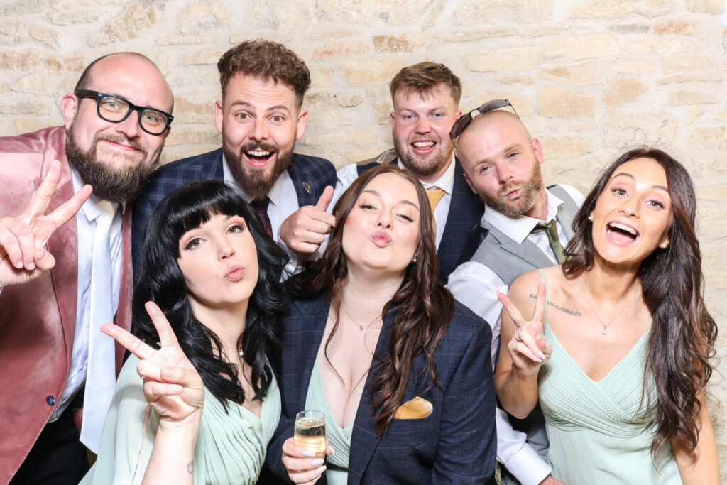 Group of wedding guests posing with peace signs at an iPad photo booth in the Cotswolds