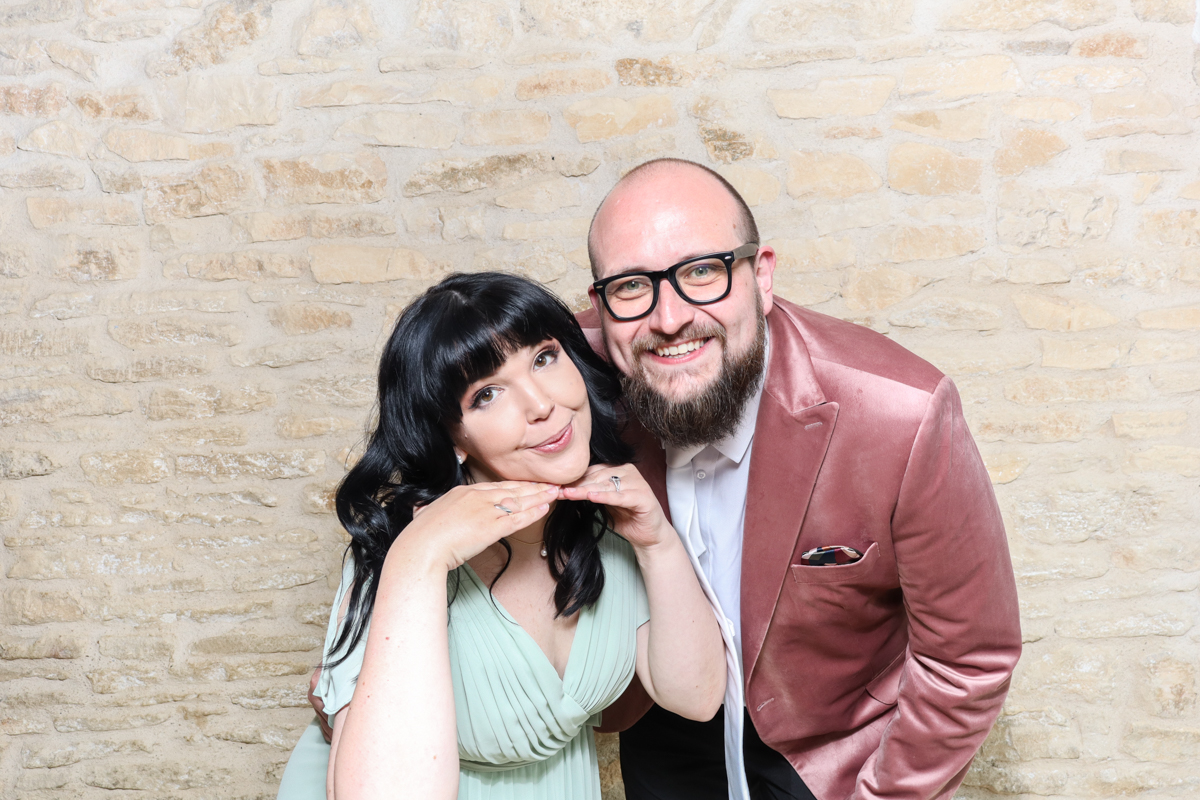 Couple posing playfully with a stone wall backdrop at a Cotswolds photo booth