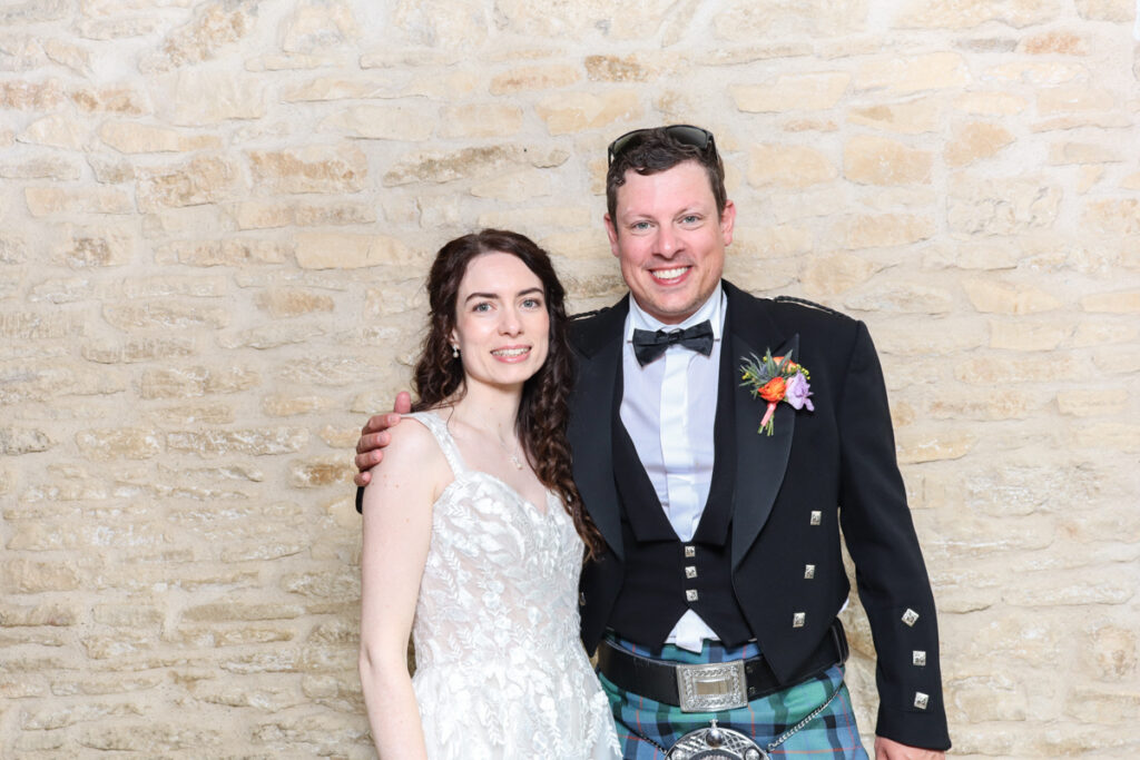 Bride and groom smiling at the camera in a wedding photo booth setup in the Cotswolds