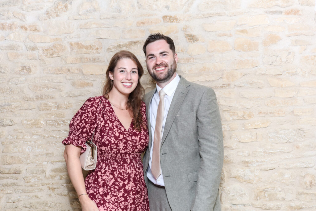 Couple dressed for a summer wedding posing in front of a stone backdrop