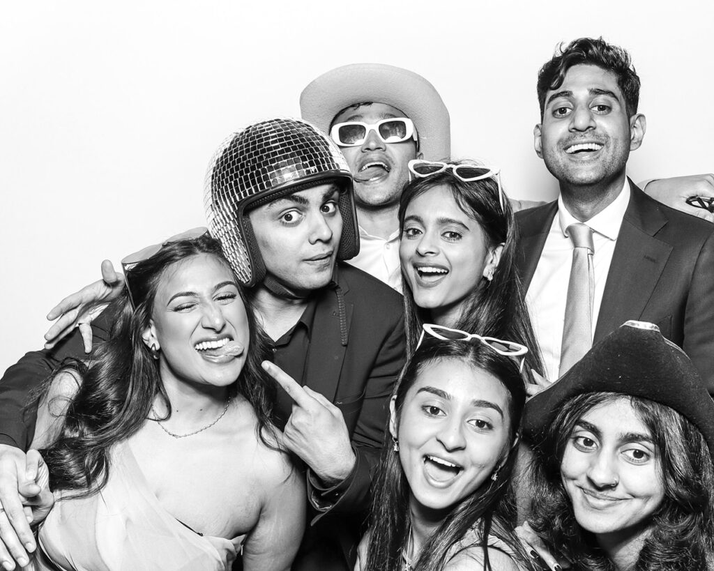 Guests laughing and posing with props inside luxury Asian weddings photo booth at evening celebration