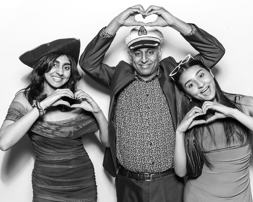 Family guests sharing the love inside luxury Asian celebration photo booth with playful hand hearts and sailor hats