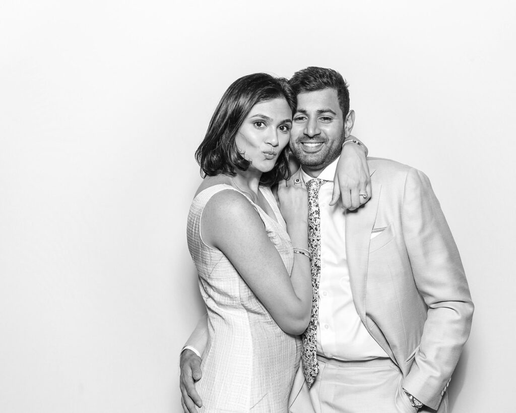 Couple sharing a relaxed and stylish pose in a Kardashian-style black and white wedding photo booth, dressed in soft-toned formalwear with confident smiles