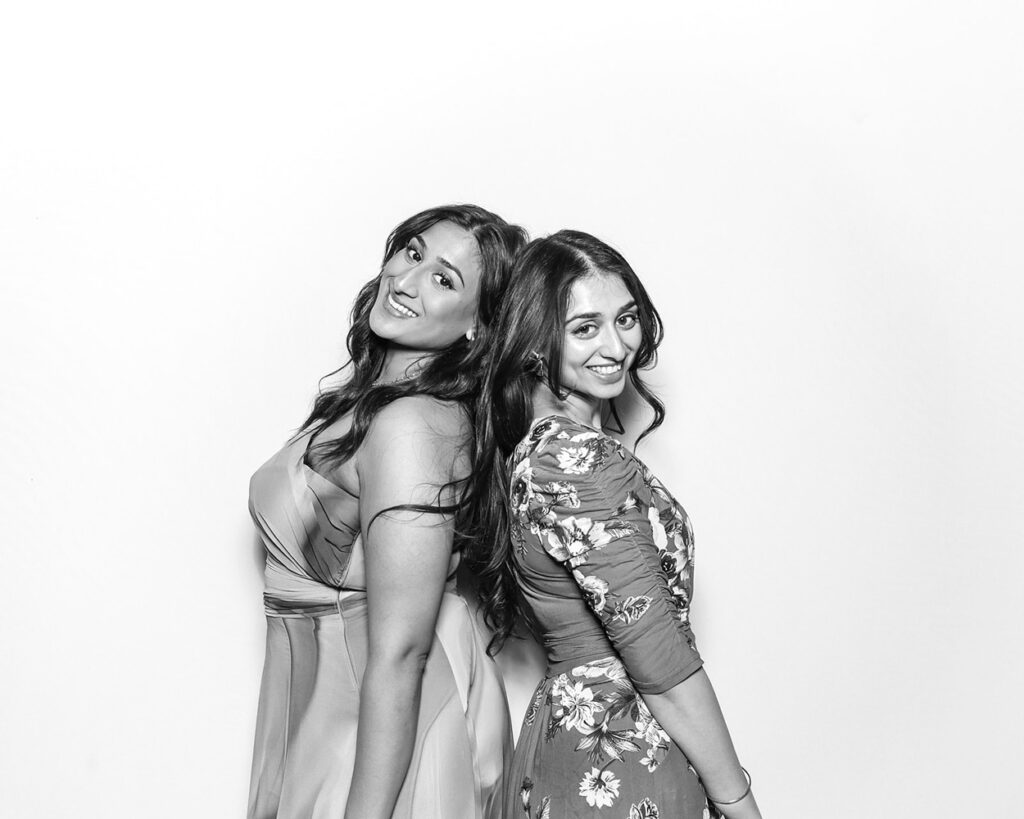 Two wedding guests posing back-to-back in elegant dresses, smiling confidently in a Kardashian-style black and white photo booth frame
