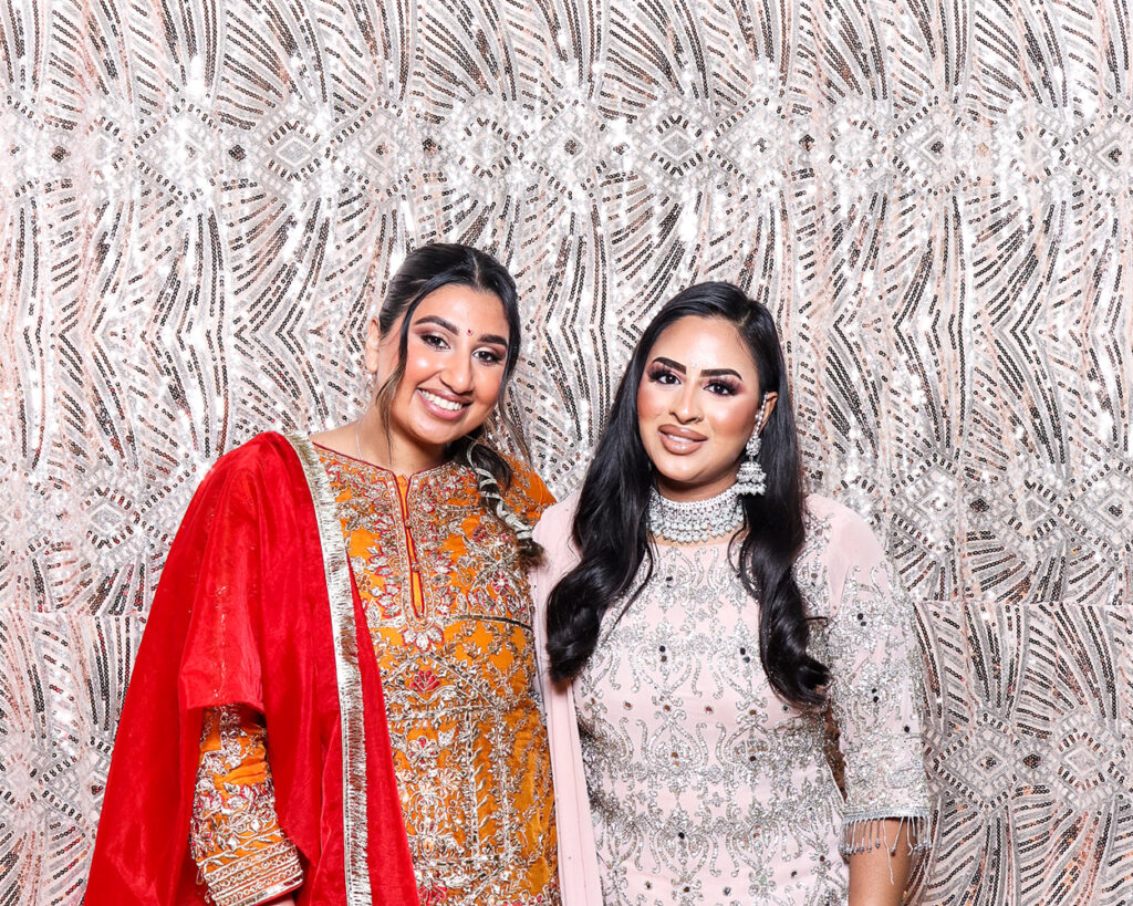 Guests dressed in elegant traditional outfits posing in a luxury Asian weddings photo booth with embellished backdrop