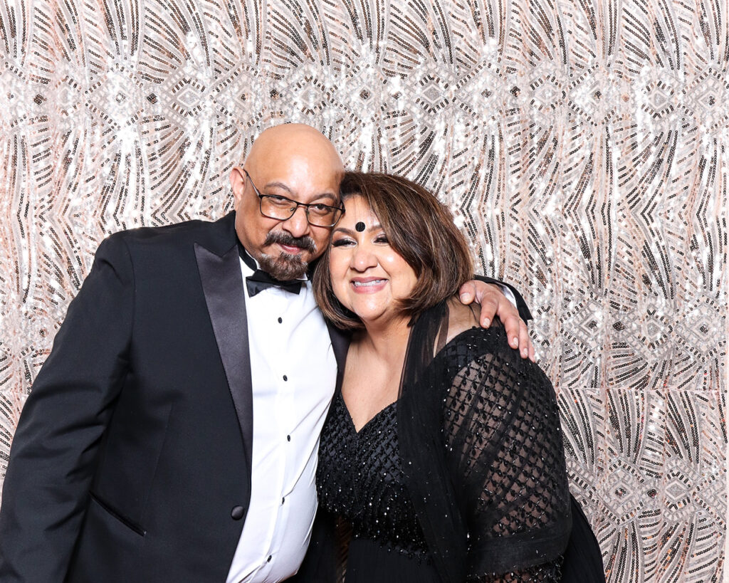 Guests in formal evening attire smiling inside luxury Asian weddings photo booth with art deco backdrop