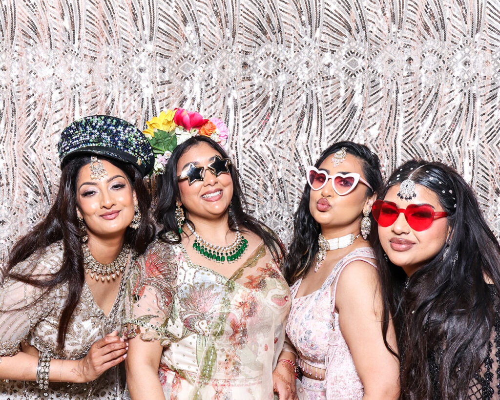 Stylish guests posing with themed props in a luxury Asian weddings photo booth during a vibrant celebration