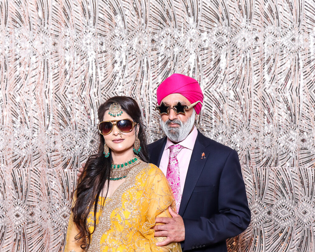 Couple making a bold fashion statement in luxury Asian weddings photo booth with star glasses and rich colors