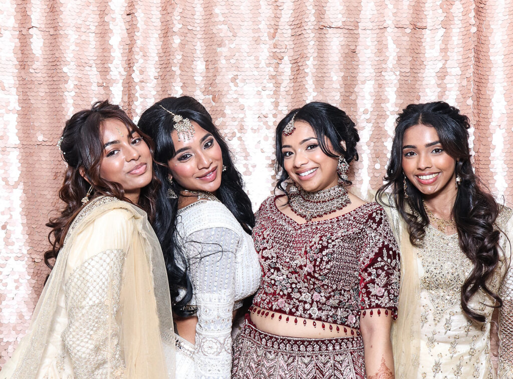 Friends posing together in luxury Asian weddings photo booth during reception with blush sequin backdrop