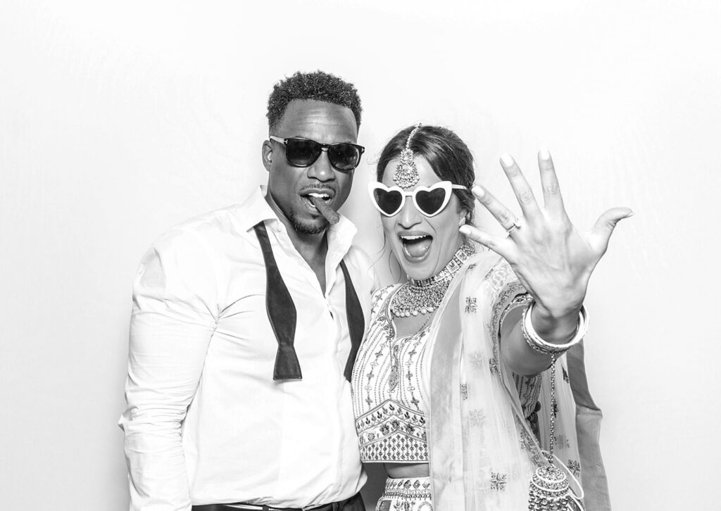 Candid moment in luxury Asian weddings photo booth with fun props and monochrome photography style for Kardashian style prints