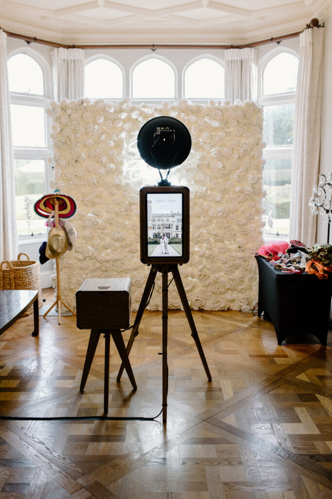 Icon photo booth setup for an asian wedding celebration, at Farleigh House with a white roses floral backdrop and a neon sign over