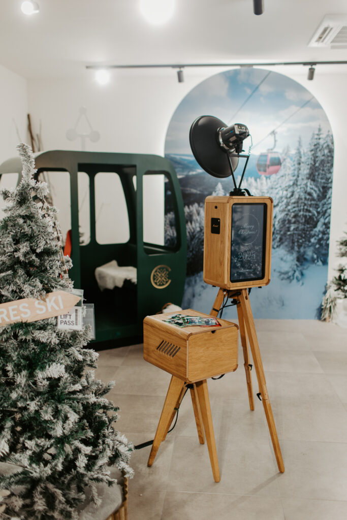 Apres ski style photo booth at Cotswolds Designer Outlet with skis, faux snow and cosy winter decor, with the wooden photo booth rental , Mad Hat Photo Booth