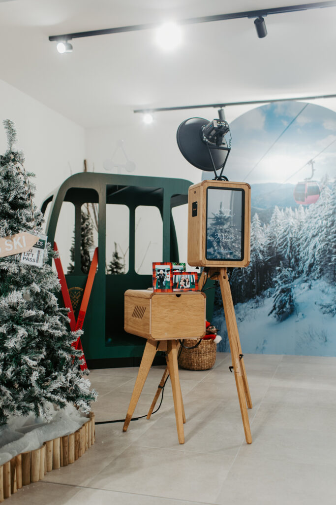 Apres ski style photo booth at Cotswolds Designer Outlet with skis, faux snow and cosy winter decor, with Christmas shopping centre photobooth wooden photo booth rental , Mad Hat Photo Booth